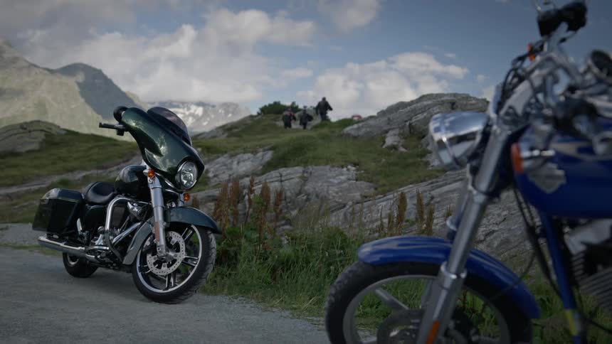 Three bikers carrying their helmets walking up a slope away from their motorcycle on the dirt road
