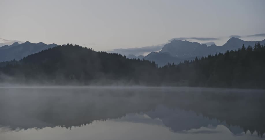 Tree covered mountain slopes and ridges reflected on the surface of a rippling lake