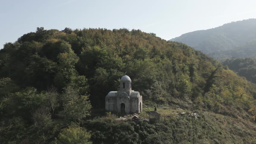 An ancient monastery isolated on top of a hill full of trees and a person is walking next to it