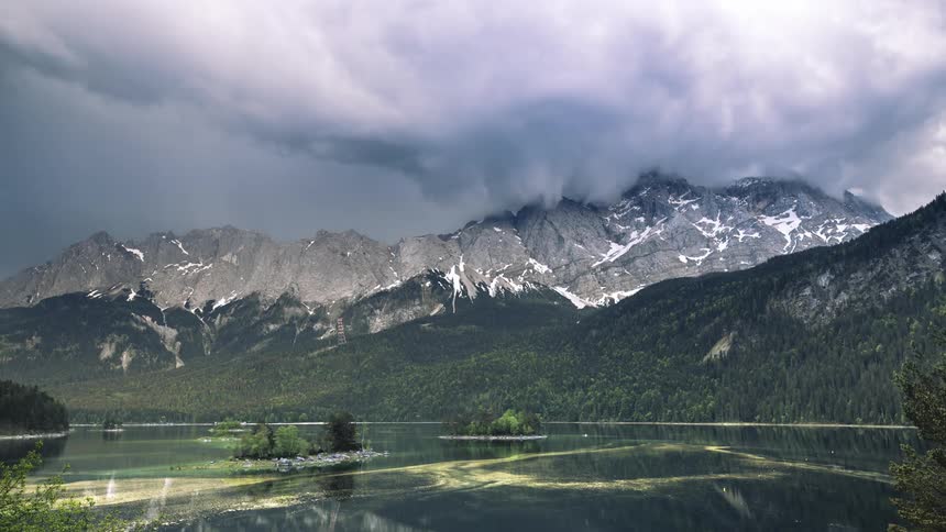 A mountain range with several gray clouds at their peak and then strong sunlight illuminates the mountain