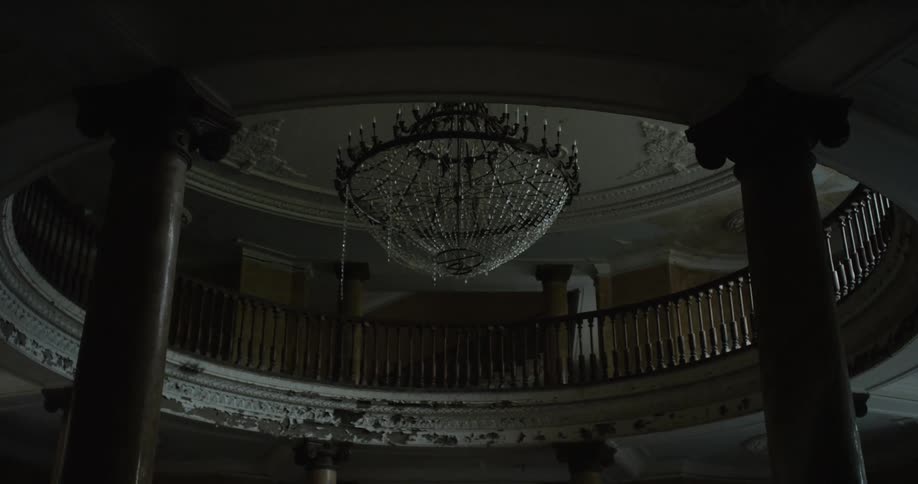 An abandoned building with a large crystal chandelier hanging in the center of a round room surrounded by columns