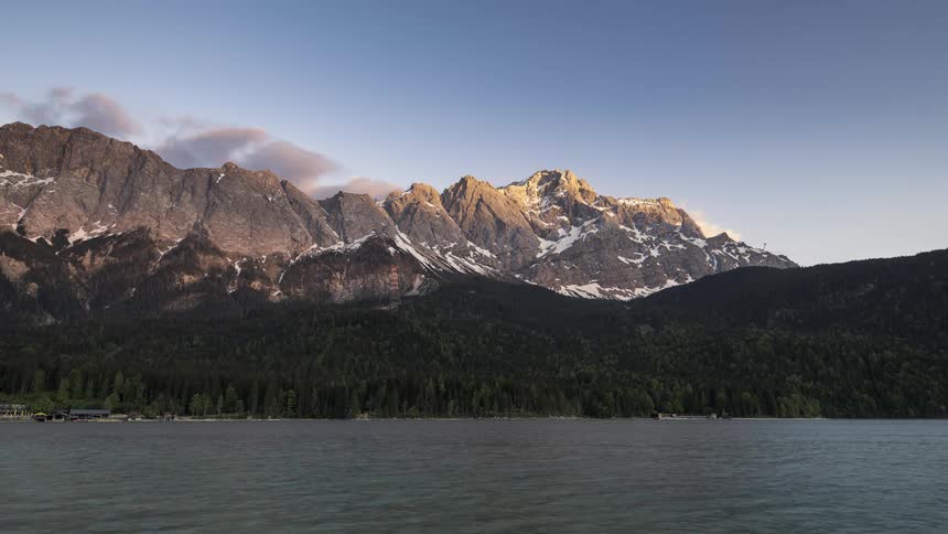 Landscape of a lake surrounded by snowy mountains with vegetation and the day is getting dark