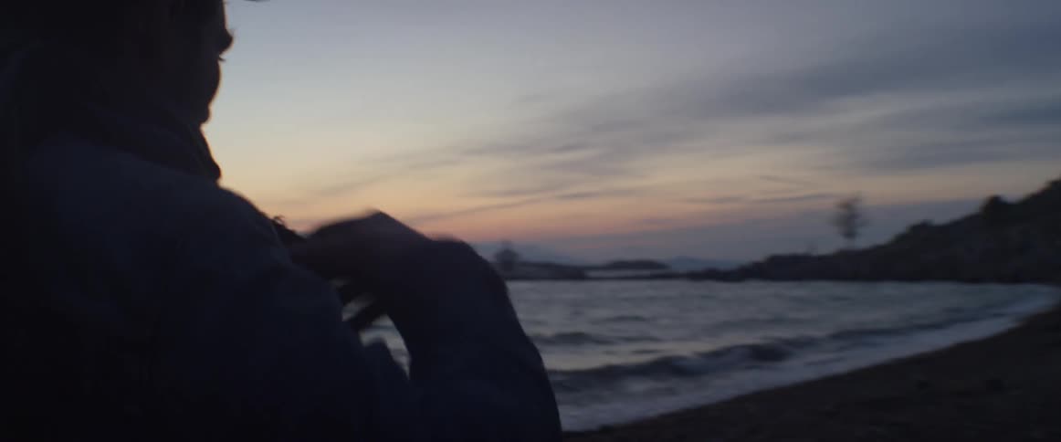 Man walking on a beach wearing a coat on a cold windy day at sunset