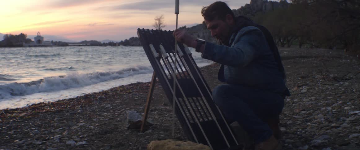 A man setting up fireworks on the shoreline as waves crash to shore on a cloudy, windy evening