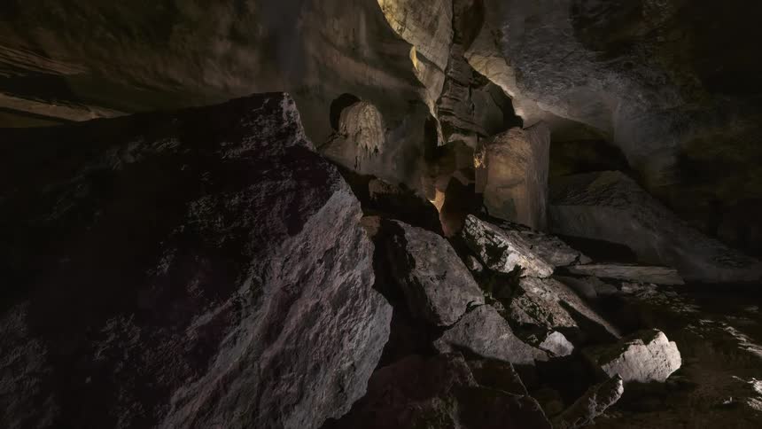 Sunlight shines onto uneven boulders resting on the floor of a large cavern