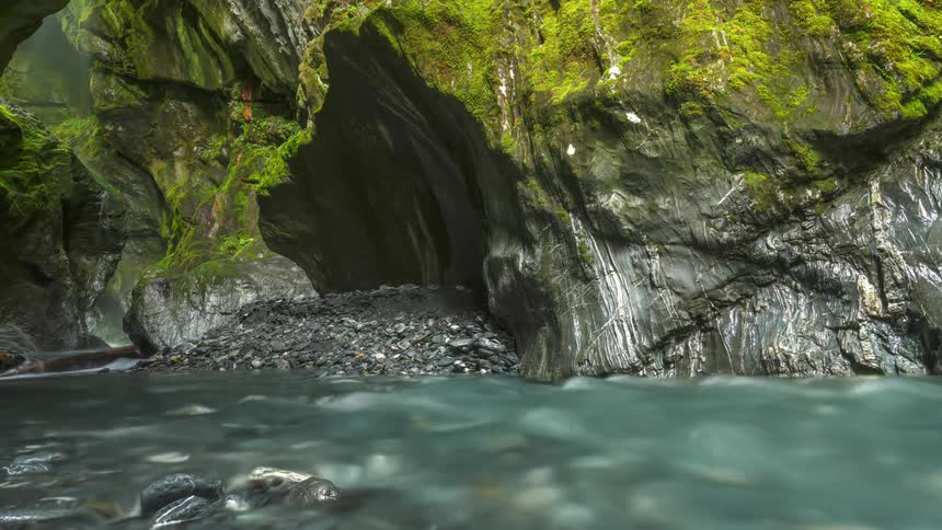 Time lapse of a natural cave surrounded by moss and a clear stream of water