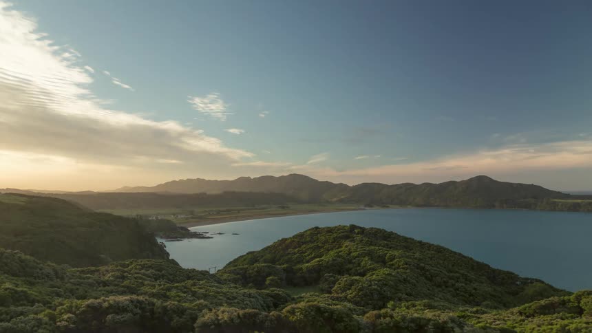 Clouds flow over forested bay coast on a sunny day
