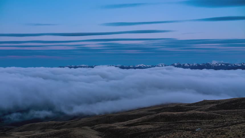 Thick fog rolls over a desert region with a mountain range in the distance