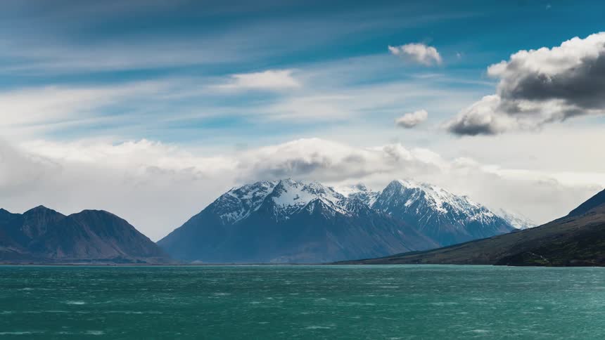 Turquoise water lake with snowcapped mountains in the background under a partly cloudy sky