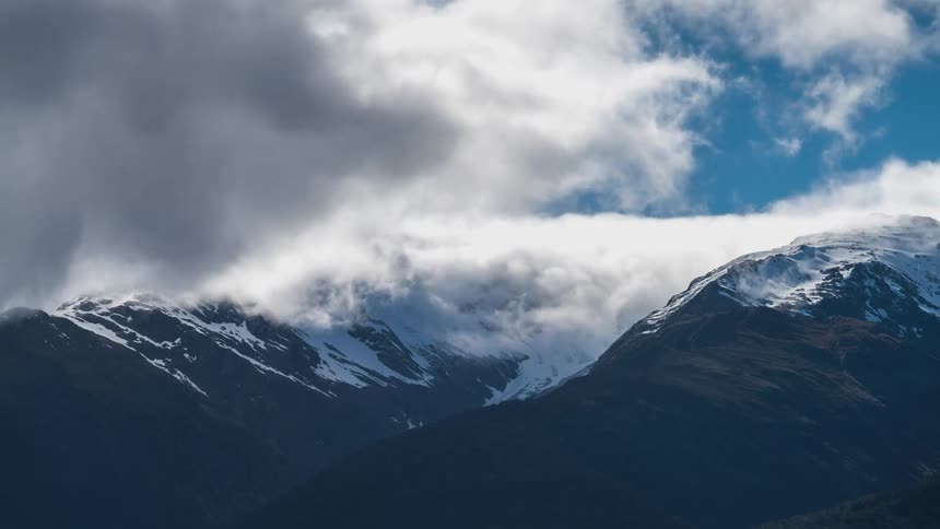 The peak of a mountain range with white clouds passing by