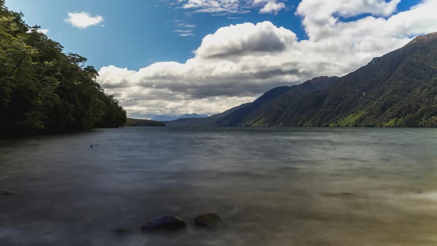 Passing clouds cast shadows onto mountain and forest separated by water