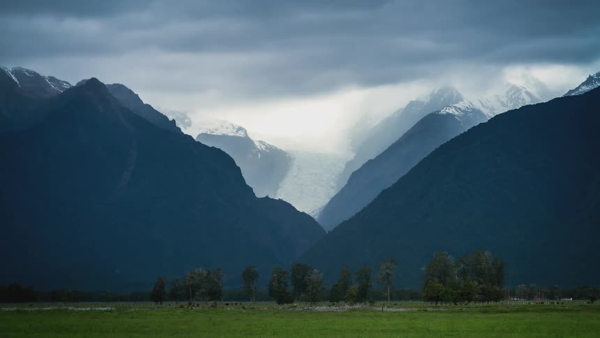 Landscape of a green field with snowy mountains in the background on a cloudy day