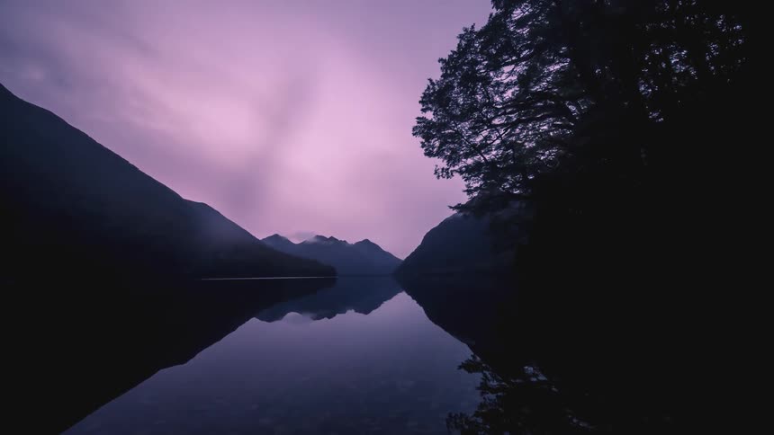 Night turns to day as dark clouds pass over a body of water in a mountain valley