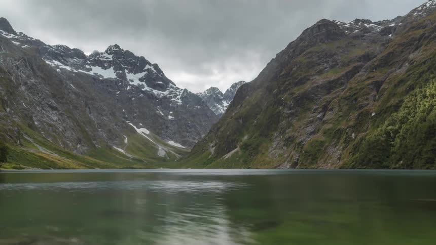 Greenish lake surrounded by snowy mountains in a cloudy sky