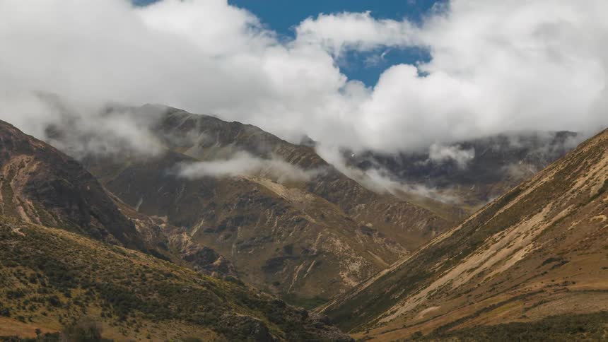 Mountain landscape with steep slopes and sparse vegetation under a partly cloudy sky