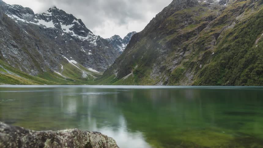 Water flows past mountains under an overcast sky