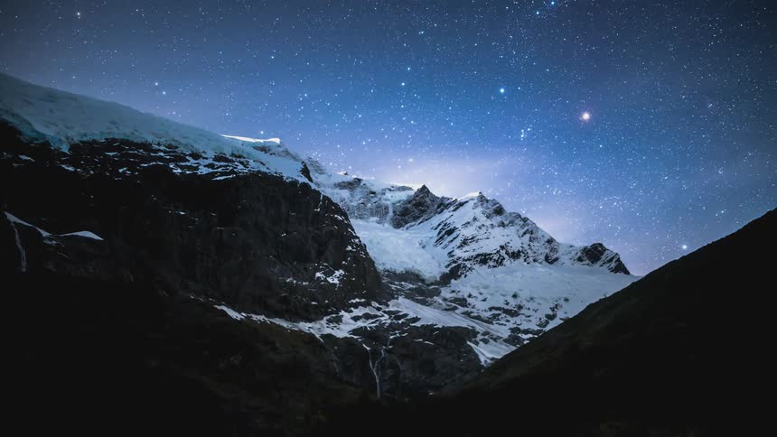 Time lapse of thin clouds rolling over a snow covered mountain range under a starry sky