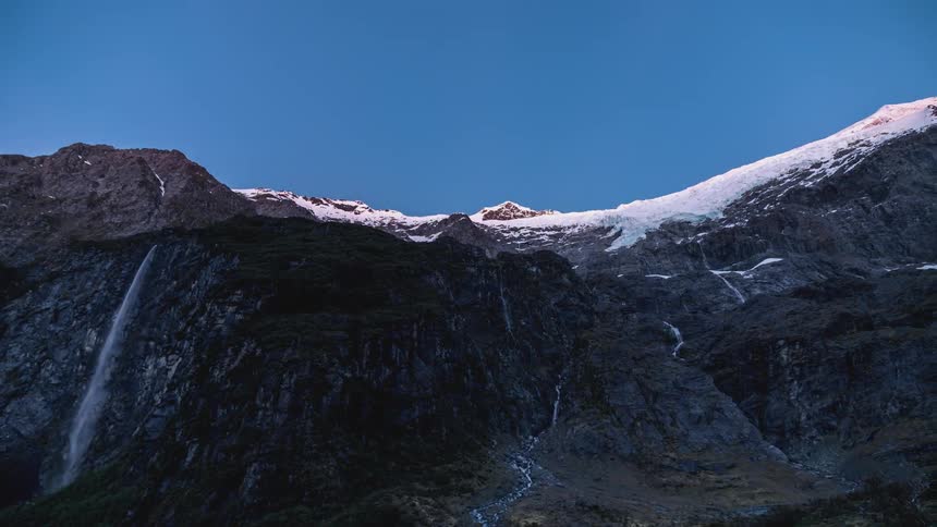 A mountain with an icy peak one night and its dawning and the sky is getting clear