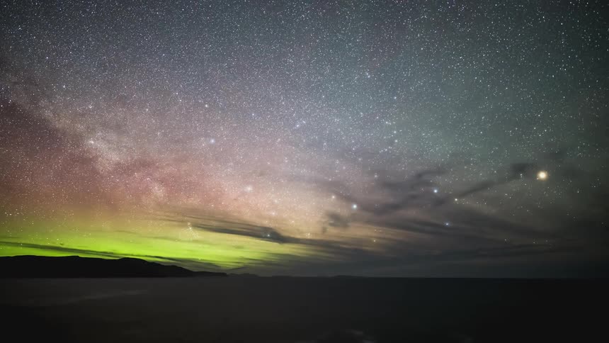 Time lapse of a starry sky and green aurora borealis over the ocean at night