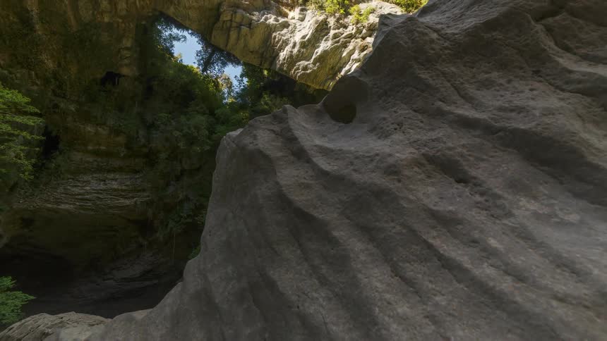 A rough rock and a hole in a huge rock full of green trees found with their