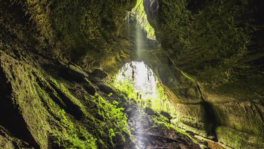 Cave with a stream flowing through it illuminated by natural light