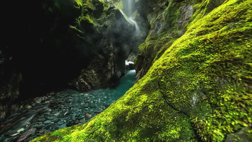 A stream with water passing through pedrinhas and large stones around it covered in moss
