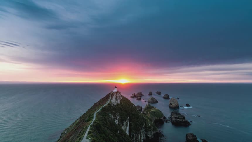 Time lapse of a lighthouse on a cliff with rocky islets in the ocean at sunset