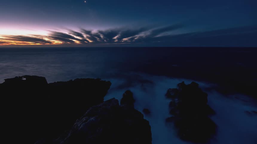 Coastal landscape at dusk with rocks in the foreground and a dramatic dusk sky