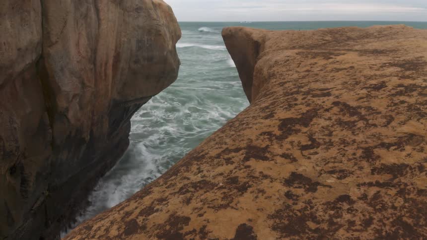 Waves flow into the narrow gap between sea side cliffs on an overcast day