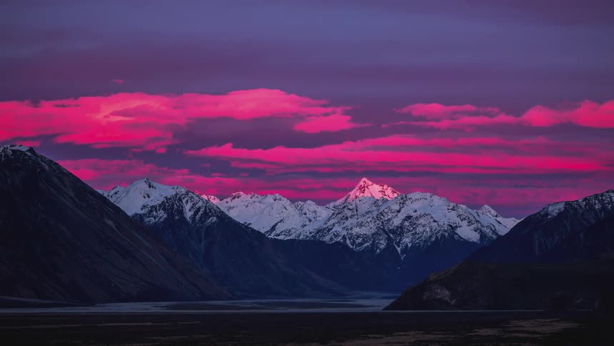Snowcovered mountain range under a dark blue sky with shades of pink and purple and the day dawning
