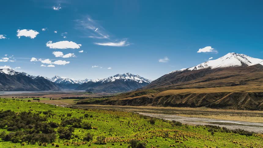 Time lapse of a landscape with green fields leading to snowcapped mountains
