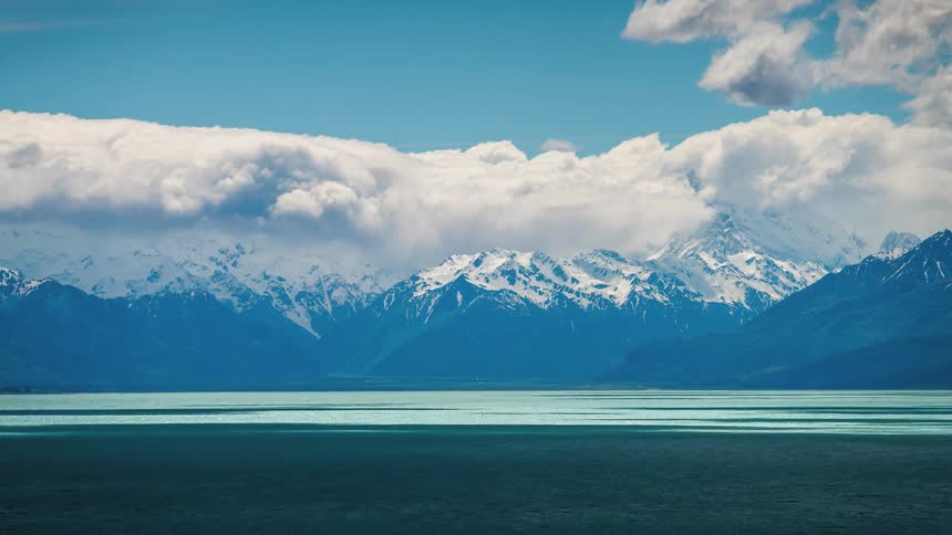 Time lapse of clouds rolling over a calm lake nested in the mountains
