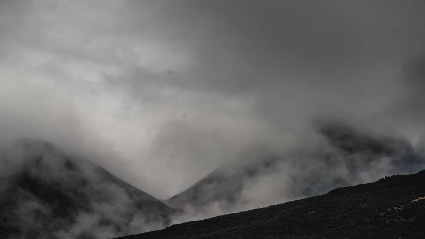 Time lapse of a thick layer of clouds rolling over the slopes of a mountain range