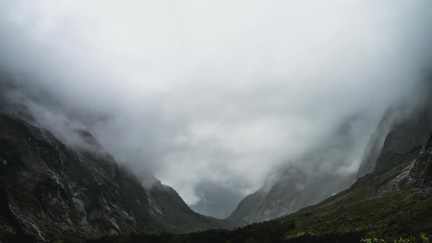Heavy low lying clouds flow through valley between mountains