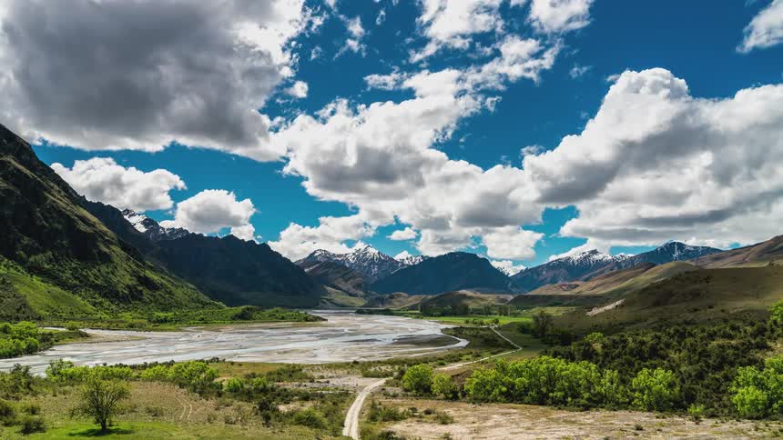 Landscape of a lake surrounded by mountains with snowcapped peaks on a blue sky day with clouds passing by