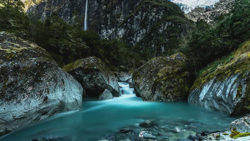 Moving blue lake surrounded by snowy mountains and clouds passing by