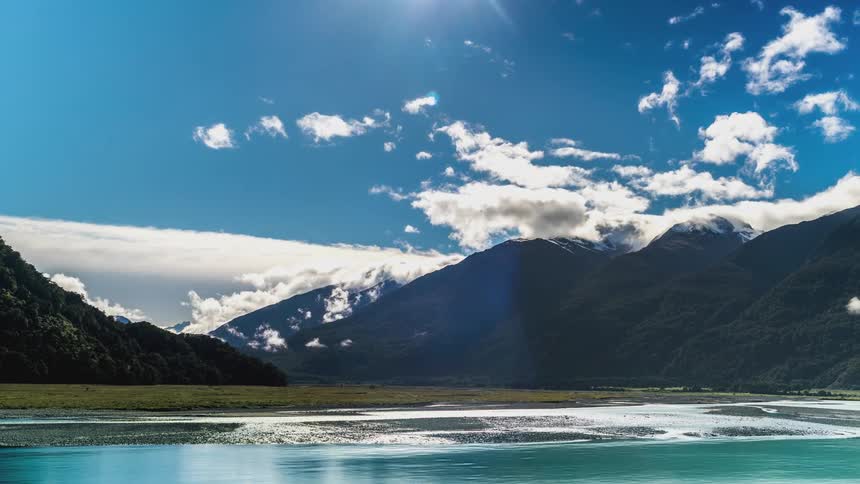 Landscape of a flowing blue lake surrounded by wooded mountains in a blue sky with clouds