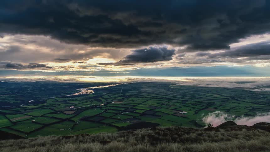 Dark storm clouds boil over a vast expanse of agricultural fields
