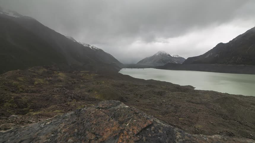 Landscape of a lake surrounded by snowy mountains against a cloudy and rainy sky