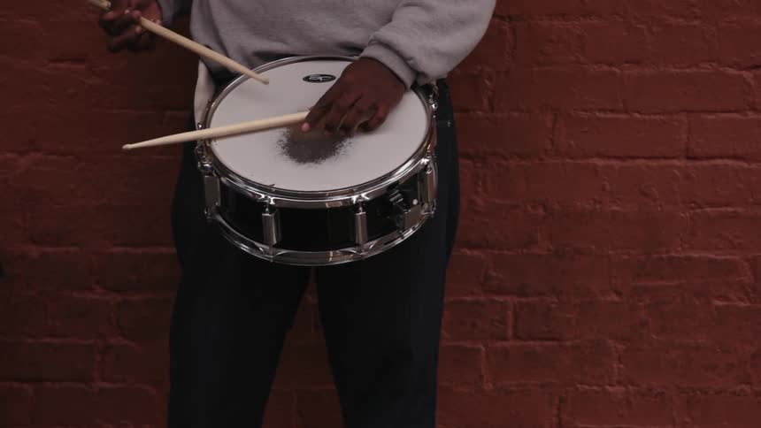 Drummer rhythmically beating his lone drum standing before a red brick wall
