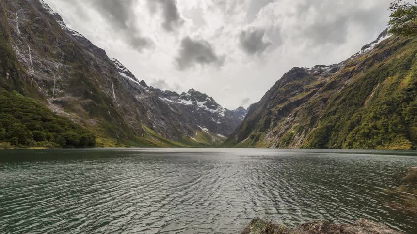 Time lapse of a mountain landscape with a lake and snowcapped peaks under the clouds