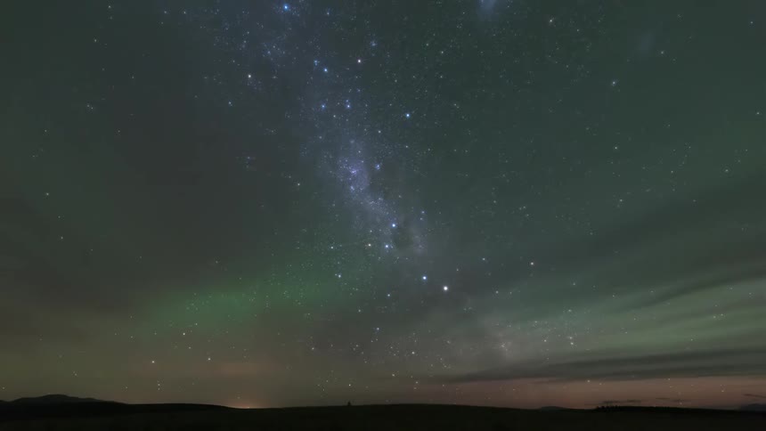 Starry night sky with the milky way and northern lights over a dark horizon