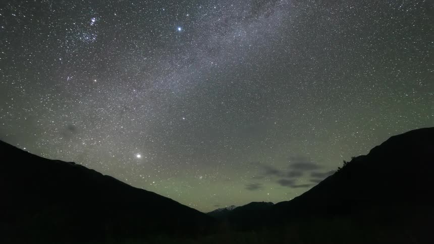 Clouds flowing over silhouetted mountains at night partially obscure a starry sky