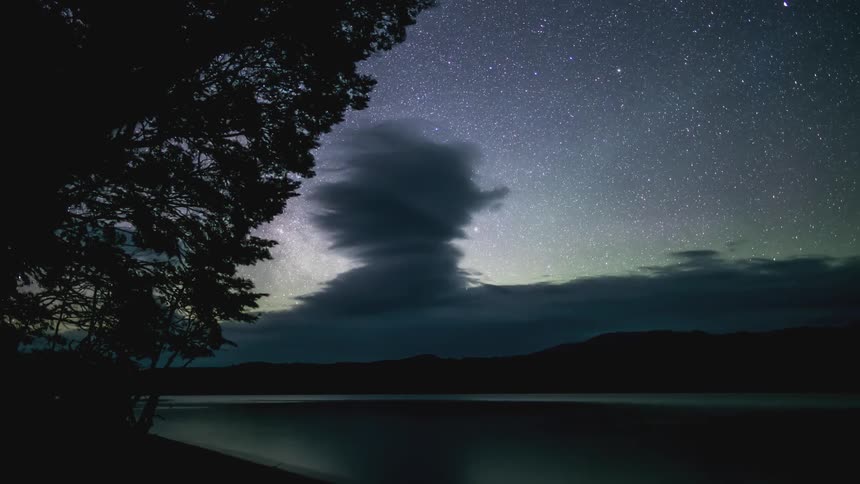 Lake waters near silhouetted mountains reflect the aurora borealis and the night sky