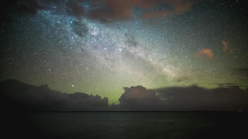 Vast ocean against a sky of stars and hazy clouds passing by