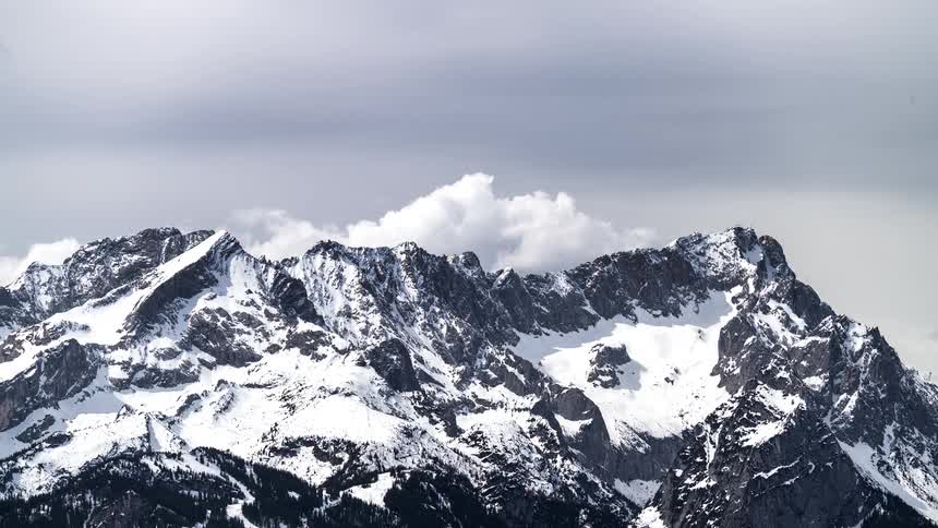 A range of some mountains covered in snow with white clouds passing in the background