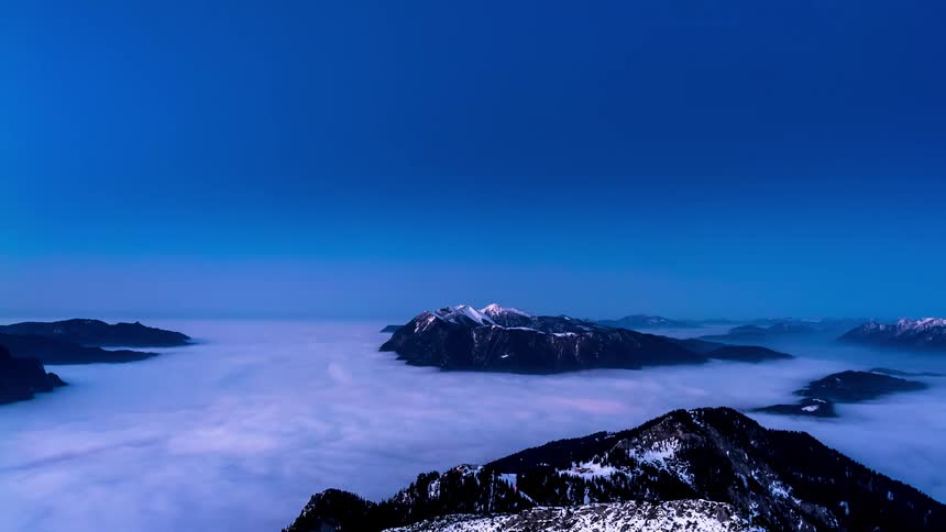 Time lapse of mountain peaks over a layer of clouds at nightfall