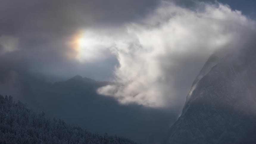 White clouds around the sky over mountains and a forest