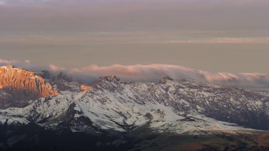 Time lapse of clouds rolling over a snow covered mountain range at sunrise