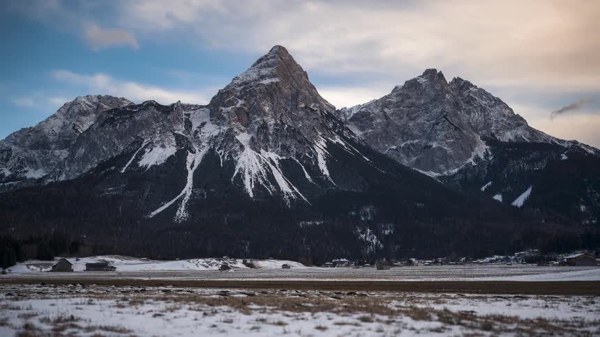 Some dark mountains with some snow on their surface and there is a rural road in front